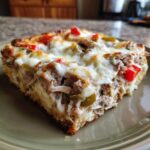 Close-up of a hearty slice of Cheesesteak casserole topped with melted white cheese, peppers, and steak filling.