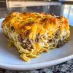 A generous slice of Cheesy Hamburger Casserole featuring ground beef, egg noodles, and a thick, browned layer of melted cheddar cheese.