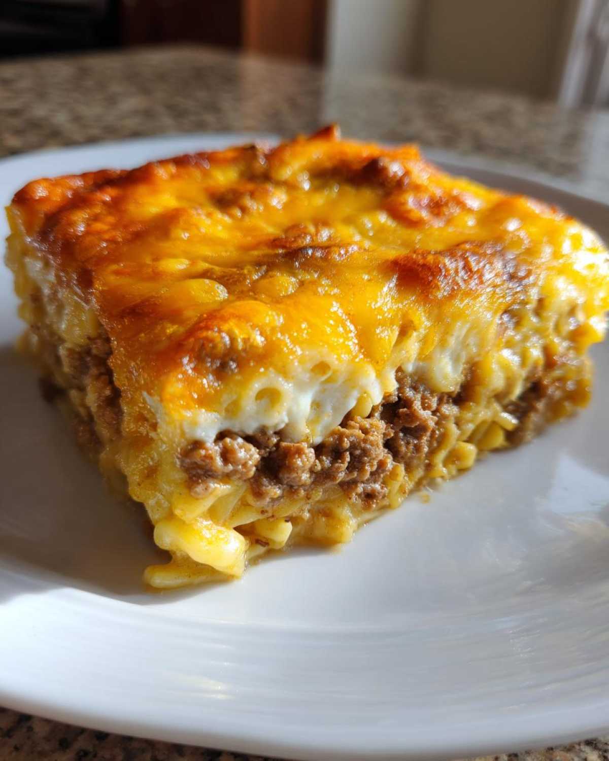 A square serving of Cheesy Hamburger Casserole showing layers of ground beef, pasta, and a bubbly, golden-brown cheese crust.