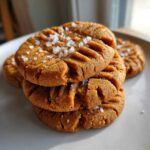 A stack of three chewy Peanut Butter Cookies topped with flaky sea salt, showing classic fork marks.