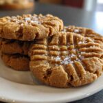 Close-up of a stack of chewy Peanut Butter Cookies, fork-pressed with sea salt sprinkled on top.