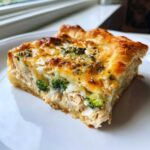 A close-up slice of golden Chicken Crescent Roll Casserole showing flaky crust, shredded chicken, and broccoli florets.