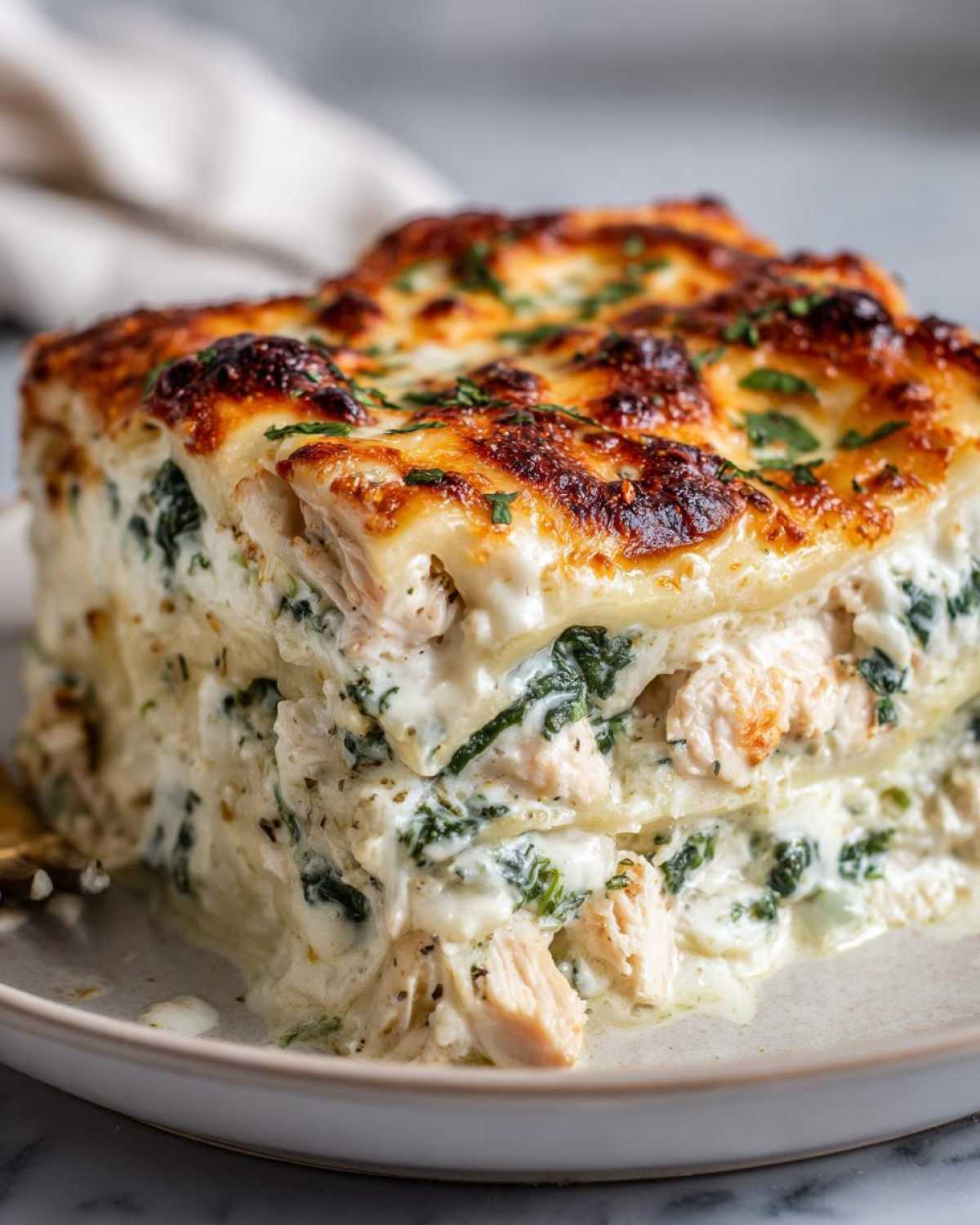 A close-up of a thick slice of Chicken Lasagna Spinach with layers of white sauce, chicken, and green spinach, topped with browned cheese.