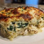 A close-up of a rich slice of Chicken Lasagna Spinach showing layers of pasta, creamy sauce, shredded chicken, and green spinach.