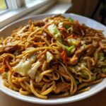 A generous serving of glossy Chicken Lo Mein noodles mixed with chicken pieces and stir-fried cabbage and carrots.