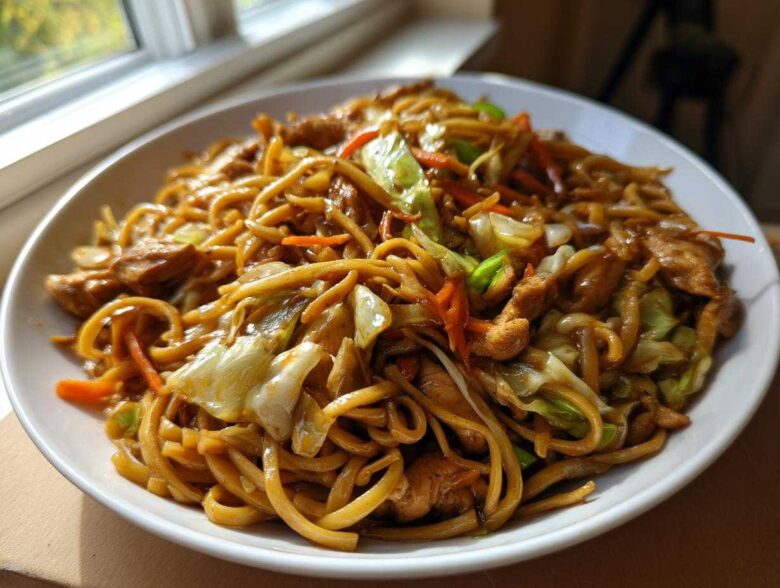 A generous serving of glossy Chicken Lo Mein noodles mixed with chicken pieces and stir-fried cabbage and carrots.