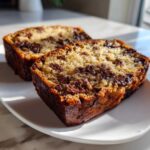 Two thick slices of moist Chocolate Chip Banana Bread with melted chocolate chunks, served on a white plate.
