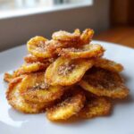 A close-up of a mound of golden brown Cinnamon Sugar Air Fryer Banana Chips dusted heavily with visible sugar crystals.