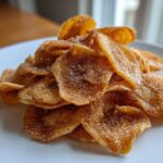 A close-up of crispy Cinnamon Sugar Air Fryer Banana Chips piled high on a white plate.