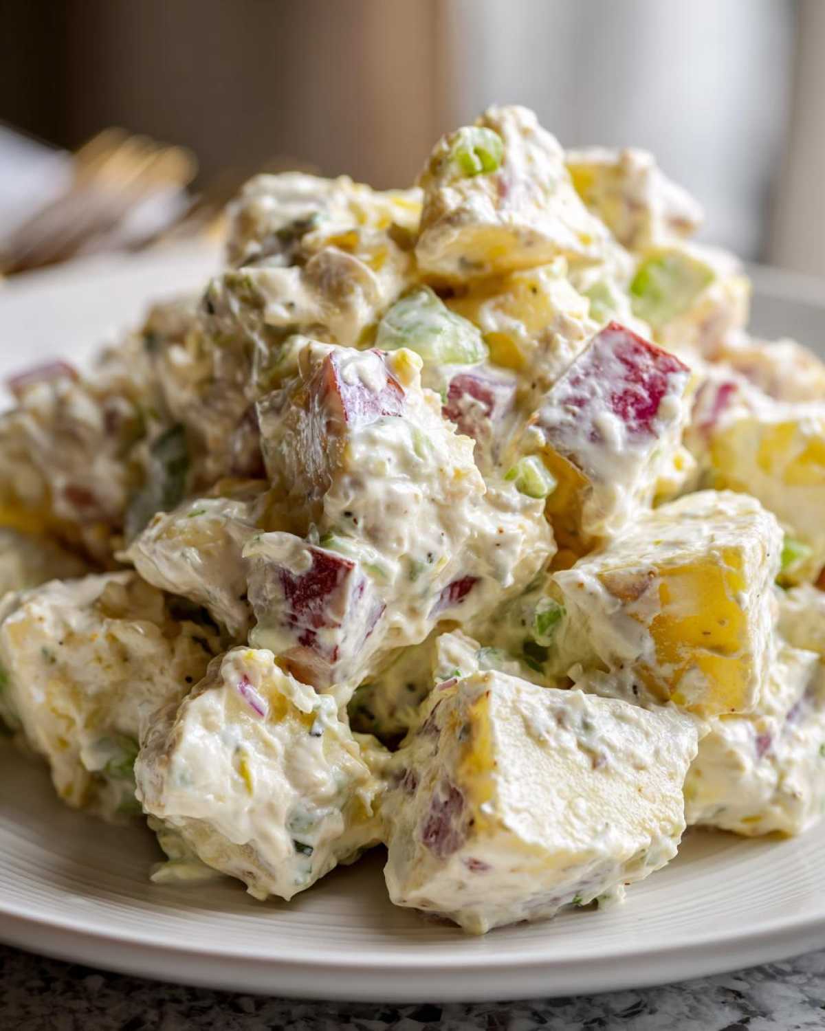 Close-up of cubed potatoes coated in creamy dressing, featuring red skins and green celery pieces in this Baked Potato Salad.