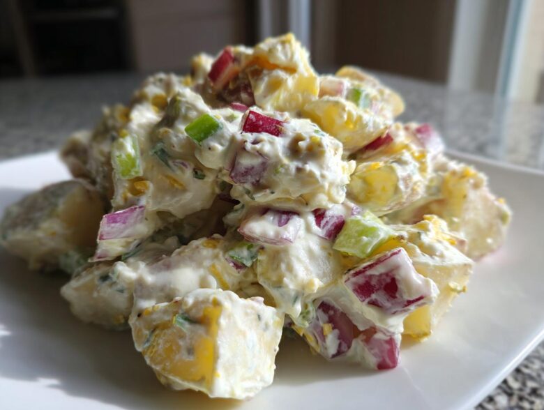 A mound of creamy Baked Potato Salad featuring chunks of yellow potato, red onion, and green celery coated in a light dressing.
