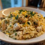 A close-up view of a serving of creamy Chicken Orzo mixed with cubed chicken breast, topped with parsley and lemon zest.