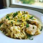 A close-up of creamy Chicken Orzo served in a white bowl, topped with fresh parsley and lemon zest.