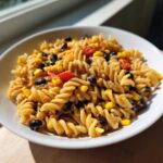 A close-up view of a serving of creamy Corn pasta salad featuring rotini pasta, black beans, corn, and diced red peppers.