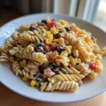 A close-up of a creamy Corn pasta salad featuring rotini pasta, yellow corn, and black beans on a white plate.