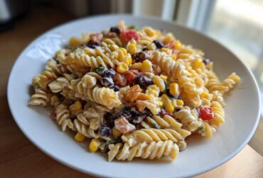 A close-up of a creamy Corn pasta salad featuring rotini pasta, yellow corn, and black beans on a white plate.