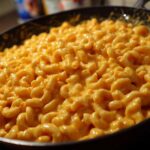 A close-up shot of rich, orange, creamy mac and cheese made with elbow macaroni, filling a dark skillet.