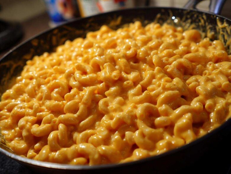 A close-up shot of rich, orange, creamy mac and cheese made with elbow macaroni, filling a dark skillet.