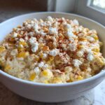 A white bowl filled with creamy Mexican Street Corn Dip, topped with crumbled white cheese and a dusting of chili powder.