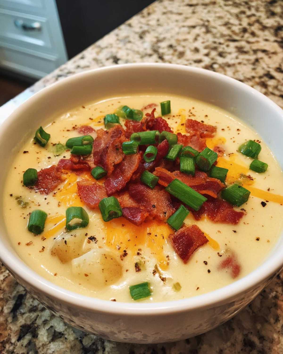 Close-up of a bowl of rich Creamy Potato Soup topped generously with crumbled bacon, shredded cheddar cheese, and fresh green onions.