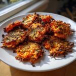 A pile of golden-brown, crispy Parmesan Ranch Smashed Carrots with visible shredded texture and green herbs on a white plate.