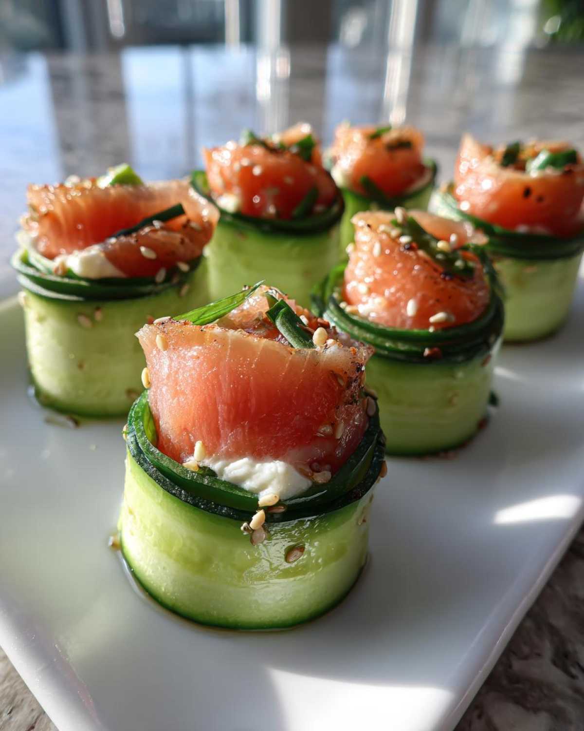 Close-up of several Cucumber Sushi rolls wrapped in thin cucumber ribbons, topped with smoked salmon, cream cheese, and sesame seeds.