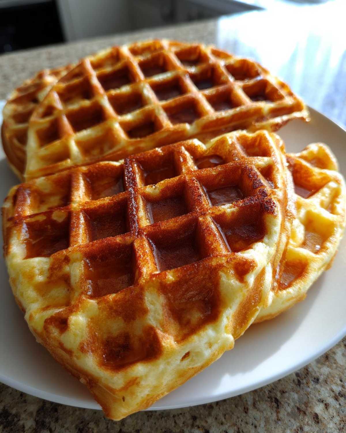 Close-up of golden brown, fluffy Belgian waffles stacked on a white plate, showing deep pockets.