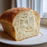 Close-up of a freshly baked loaf of Homemade Bread, showing a fluffy, white interior crumb and golden-brown crust.
