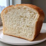 A close-up of a thick, fluffy slice of homemade bread showing its soft white crumb and golden crust.
