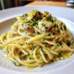 A close-up of a serving of Fresh Lemon Chicken Pasta tossed in a creamy sauce, topped with chicken pieces, parsley, and lemon zest.