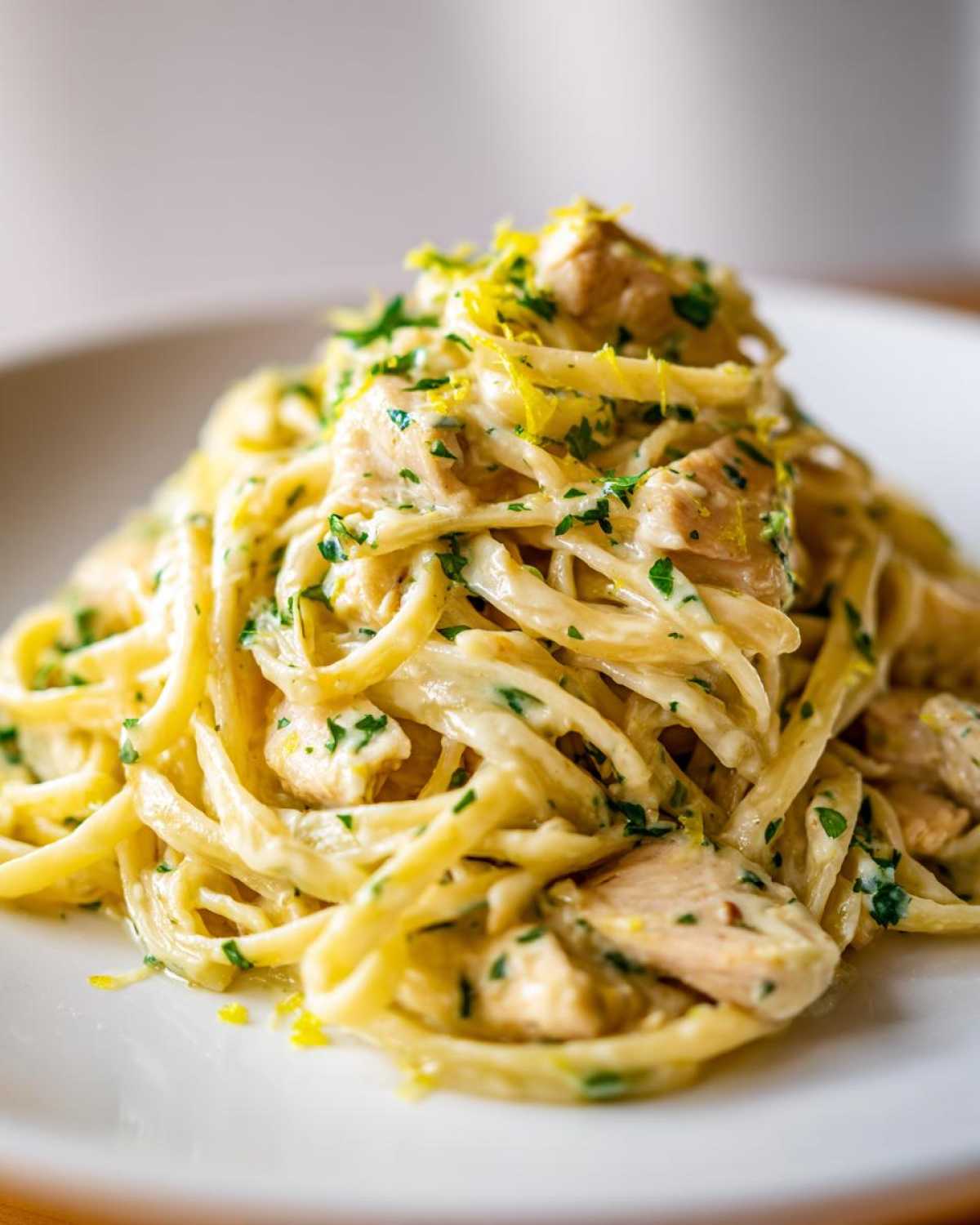 A close-up of creamy Fresh Lemon Chicken Pasta tossed with chunks of chicken, parsley, and bright lemon zest.