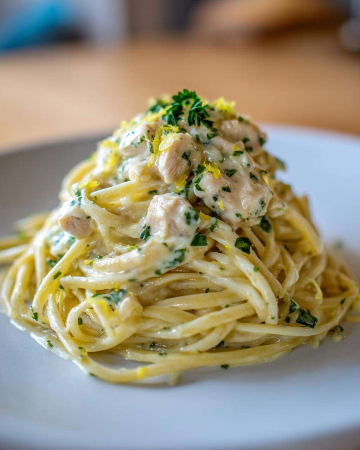 A close-up of a serving of Fresh Lemon Chicken Pasta, topped with diced chicken, creamy sauce, lemon zest, and fresh parsley.