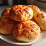A pile of golden brown, freshly baked pepperoni pizza bites topped with melted cheese on a white plate.