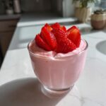 A glass cup filled with pink Fresh Strawberry Mousse, topped with sliced fresh strawberries.