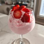 A glass of pink, airy Fresh Strawberry Mousse topped with sliced fresh strawberries.