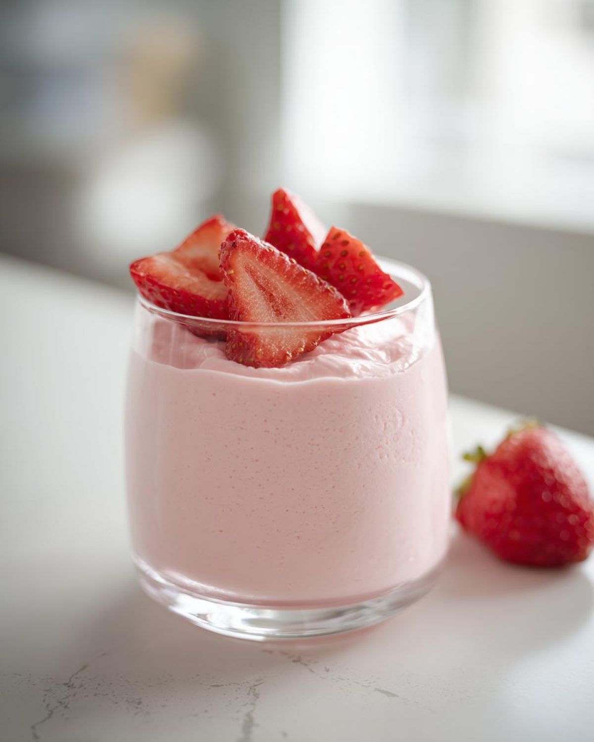 A glass filled with light pink Fresh Strawberry Mousse, topped with fresh strawberry slices.