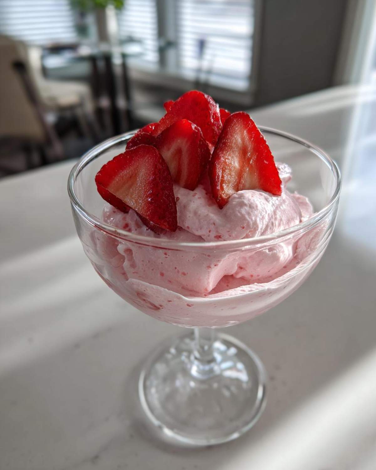 A glass coupe filled with light pink Fresh Strawberry Mousse, topped with sliced fresh strawberries.