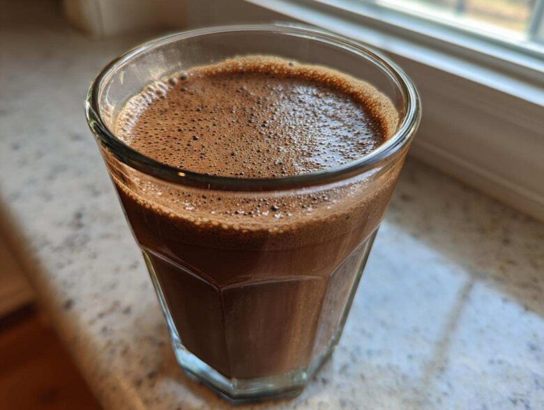 Close-up of a freshly blended, frothy Coffee Smoothie in a clear glass resting near a window.