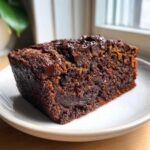 A close-up of a rich, dark slice of Fudgy Chocolate Banana Bread topped with melted chocolate chips.