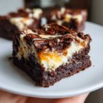 Close-up of a fudgy Gluten Free Cheesecake Brownies square with a thick cheesecake layer and caramel swirl.