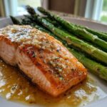 Close-up of a perfectly cooked fillet in a Garlic Butter Baked Salmon Dinner, topped with minced garlic sauce and served alongside bright green asparagus.