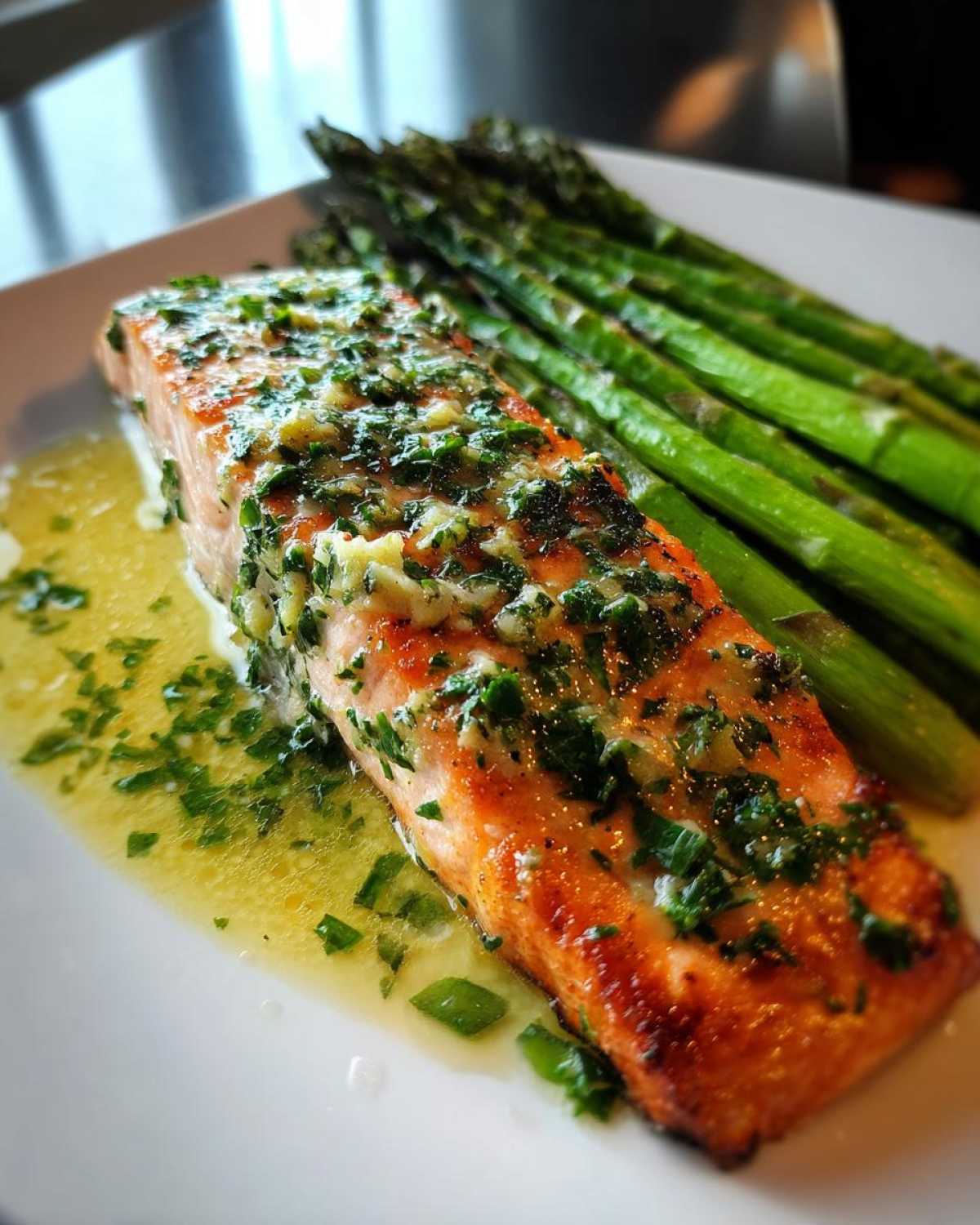 Close-up of a perfectly cooked Garlic Butter Baked Salmon Dinner topped with herbs, served next to roasted asparagus.