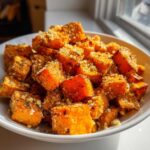 Close-up of roasted sweet potatoes cubes topped with grated cheese and herbs, ready to eat.