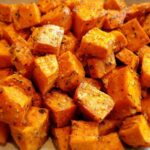 Close-up of bright orange, cubed Garlic Parmesan Roasted Sweet Potatoes coated in herbs and spices.