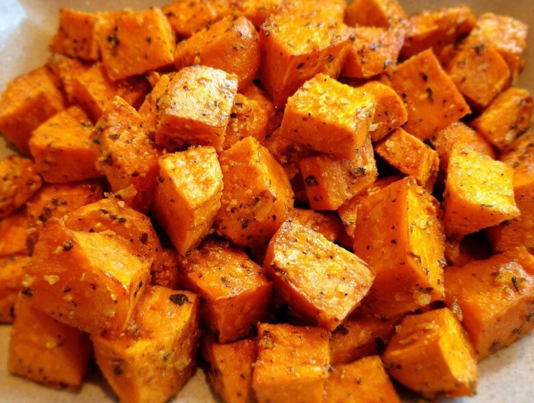 Close-up of bright orange, cubed Garlic Parmesan Roasted Sweet Potatoes coated in herbs and spices.
