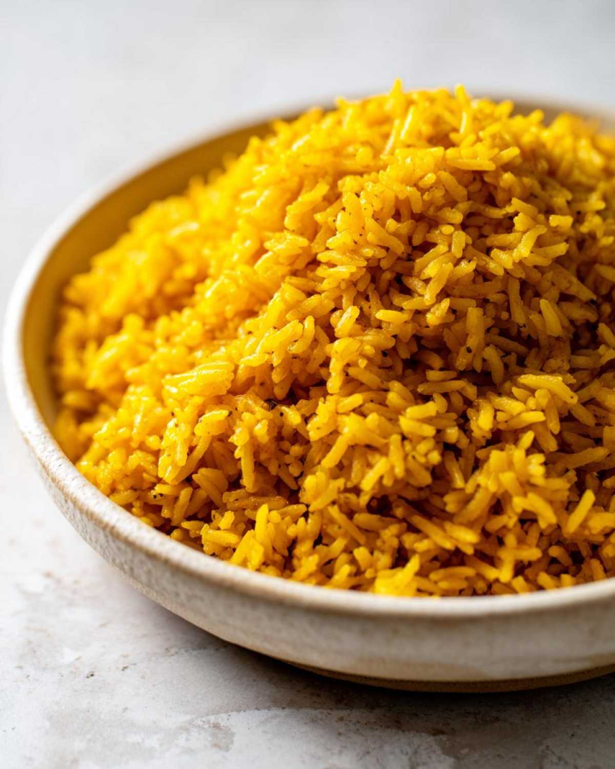 Close-up of fluffy, bright yellow Garlic Turmeric Rice served in a light-colored ceramic bowl.
