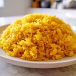 A mound of vibrant yellow Garlic Turmeric Rice served on a simple white plate.