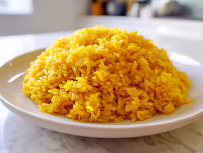 A mound of vibrant yellow Garlic Turmeric Rice served on a simple white plate.