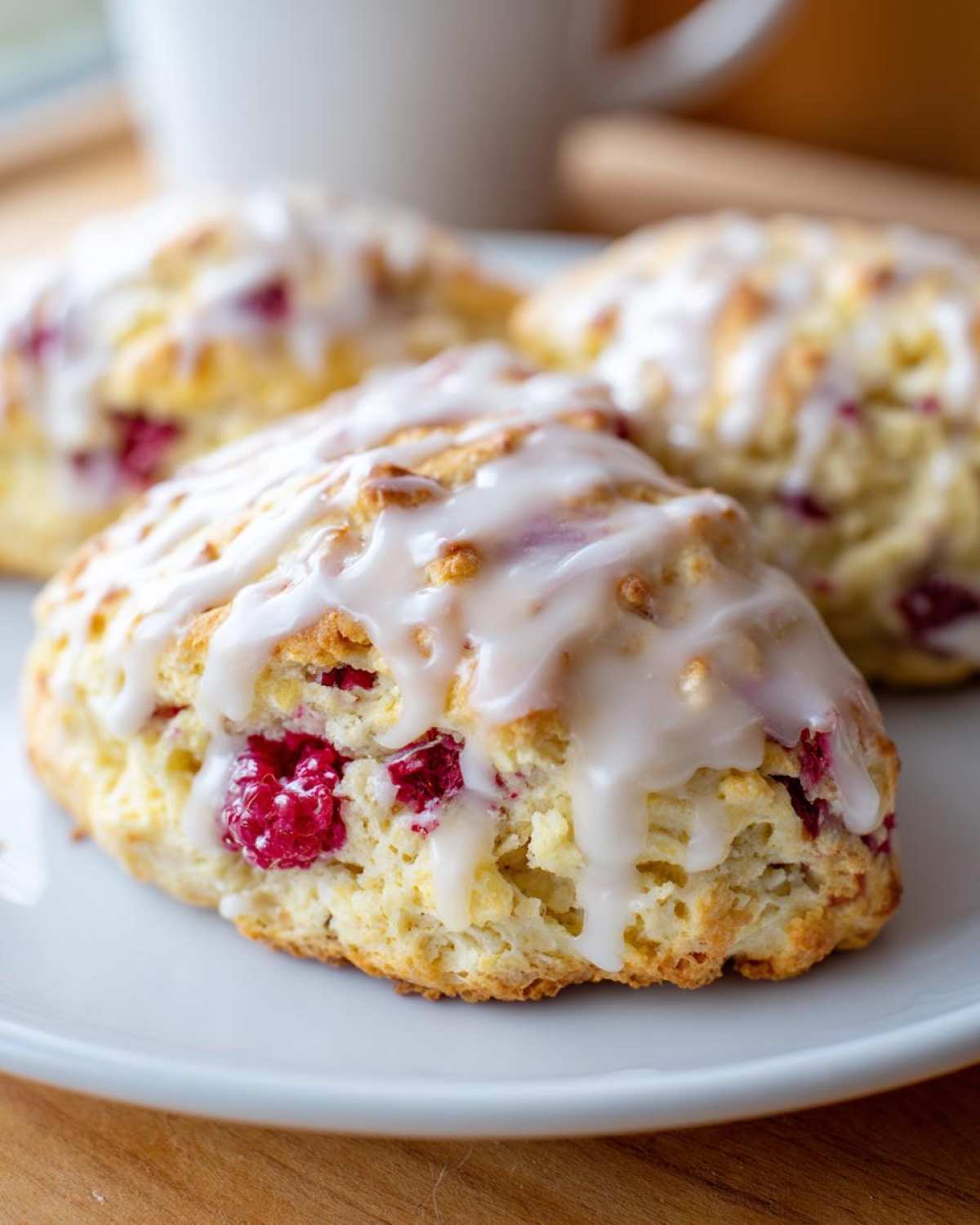 A close-up of a freshly baked Lemon Raspberry Scones, topped with a thick white glaze, sitting on a white plate.