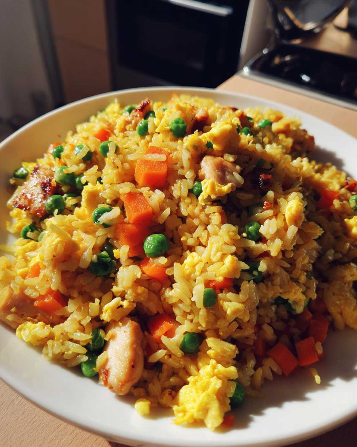 Close-up of a white plate piled high with golden Chicken Fried Rice, featuring scrambled egg, peas, and diced carrots.